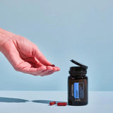 dōTERRA Adaptiv Nahrungsergänzung – Hand hält offene Flasche mit roten Kapseln vor blauem Hintergrund | doTERRA